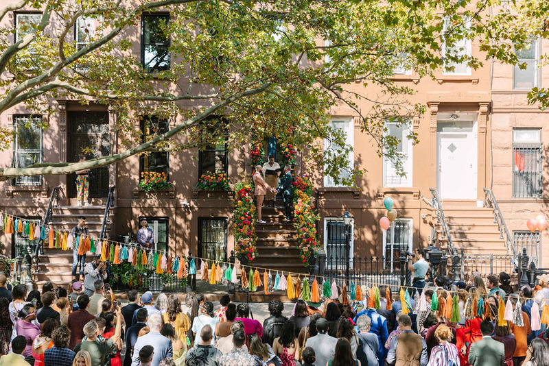 Distant view of Celebrant Lauren Hill officiating the wedding of Barry Bordelon and Jordan Slocum, the Brownstone Boys. The street is filled with neighbors and friends dressed in colorful clothes