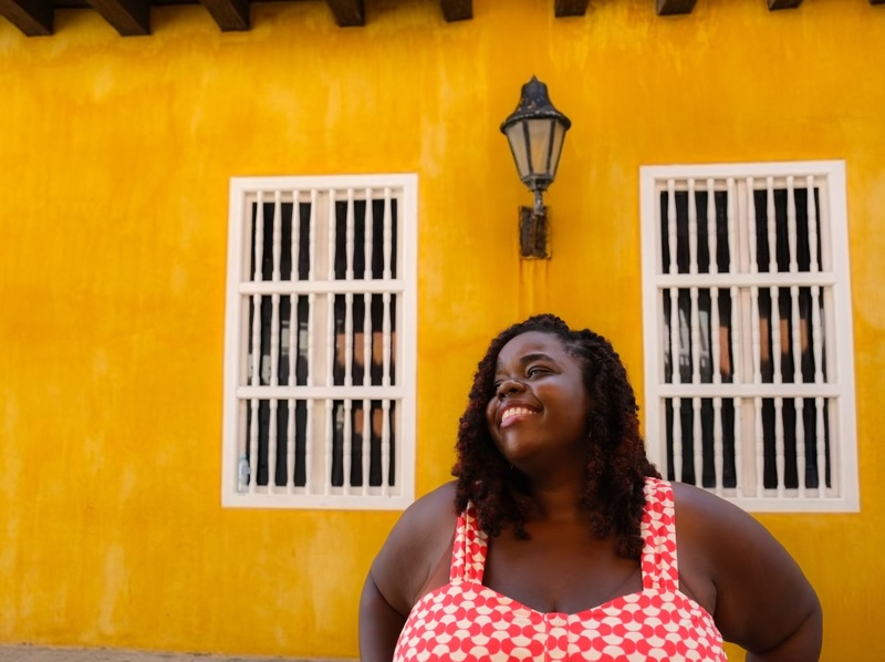 Wedding Celebrant Lauren Hill poses against a bright yellow wall, smiling 