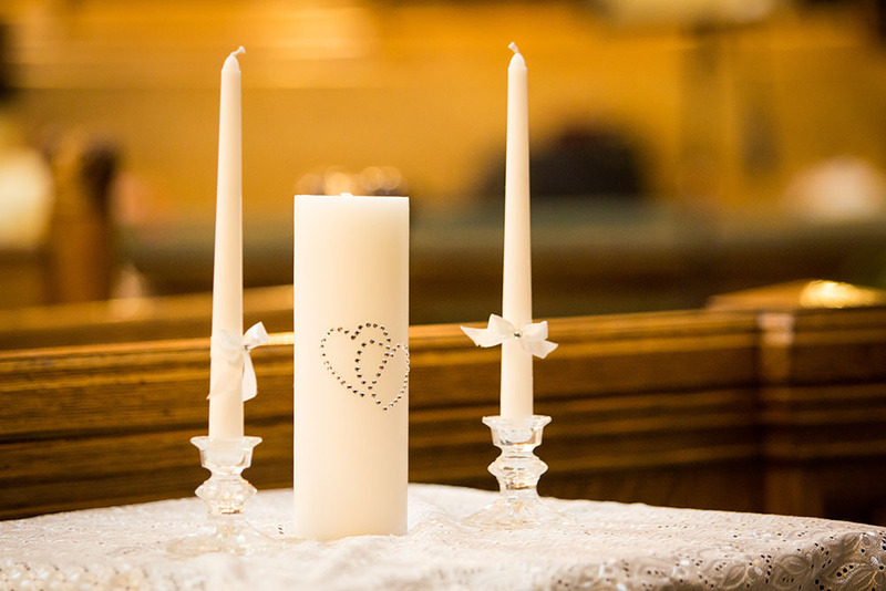 Close up of a the unity candle ceremony supplies, showing two small taper candles and a larger unity candle with rhinestones in the shape of two interlocking hearts