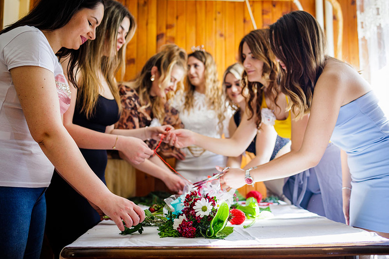 bridesmaids working together on wedding wreaths, lined up along a long wooden table with materials and flowers on the center