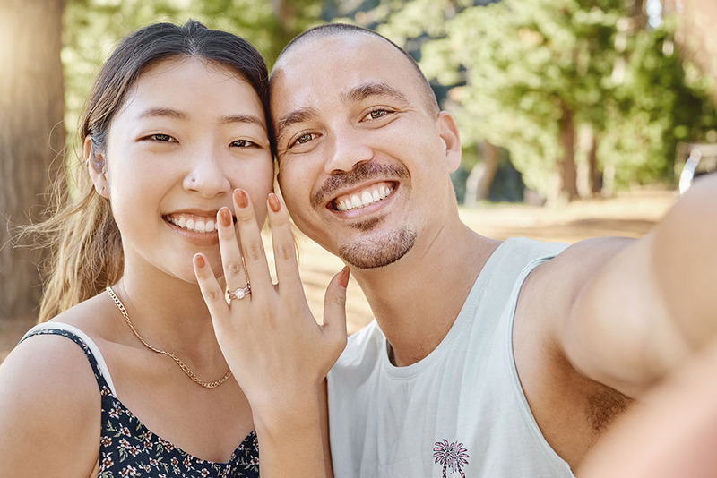 Newly engaged couple smile and show off the ring in an engagement ring selfie