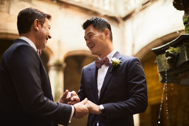 Two grooms hold hands and smile happily at the wedding