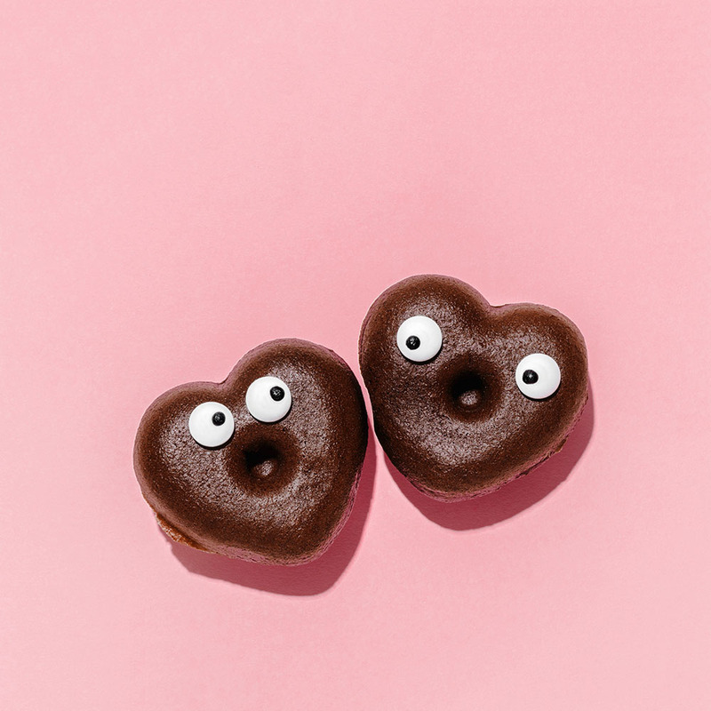 Two heart shaped donuts with googly eyes against a pink background