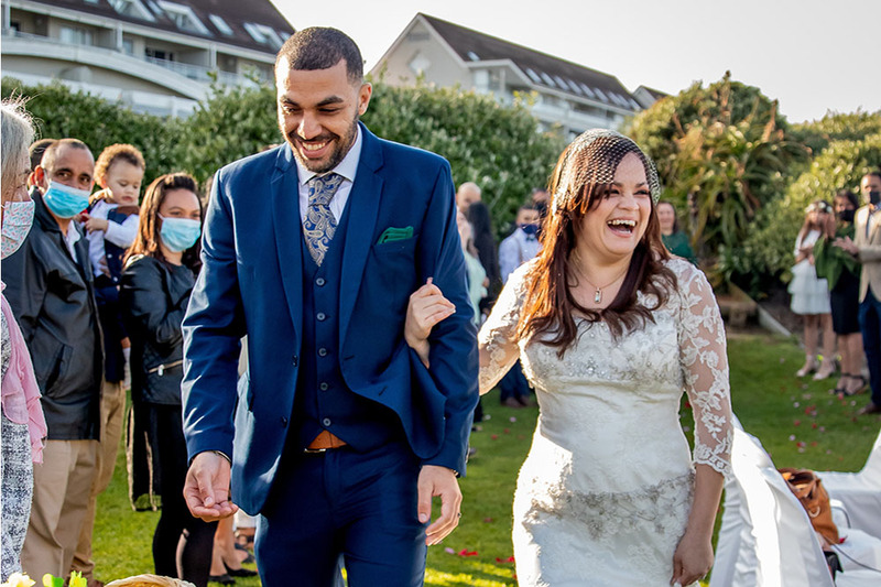 Bride and groom walk down the aisle laughing happily while friends and family watch