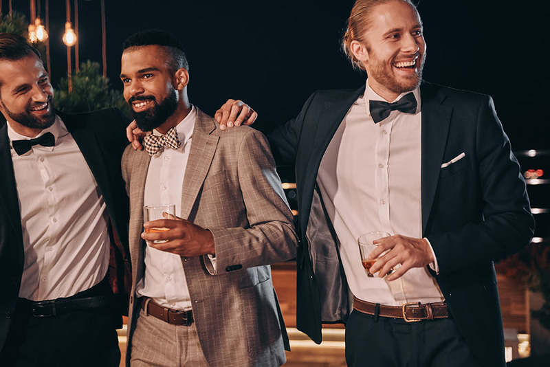 Wedding officiant, groomsman, and groom stand together at the wedding reception looking happy 