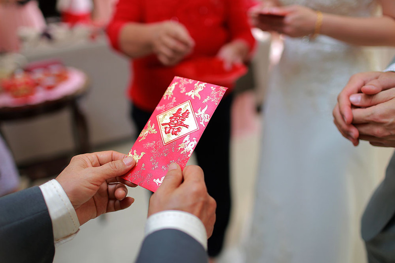 Close up of a wedding guest holding a decorative red envelope to give the wedding couple a cash gift during the tea ceremony