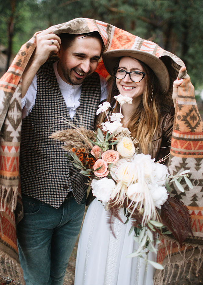 Two young newlyweds pose under a blanket on the wedding day