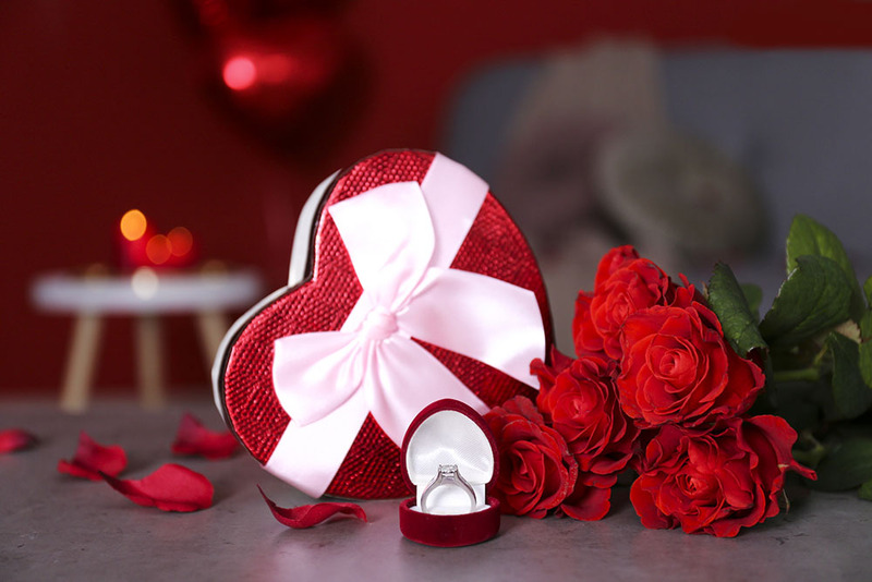 Valentine's candy in a heart shaped box next to an engagement ring or wedding ring