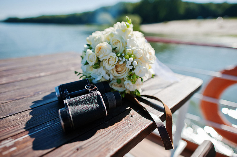 Birdwatching binoculars next to a wedding bouquet on a picnic table outdoors