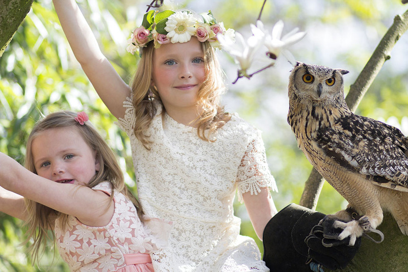 Two flower girls pose with a wedding owl at an outdoor wedding
