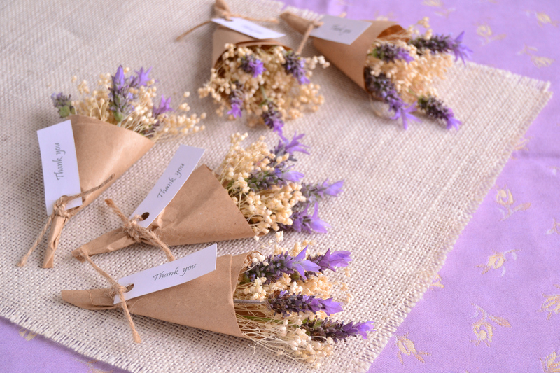 Bundles of lavender and dried flowers for summer solstice wedding favors, wrapped in light brown paper with small tags that read 'thank you' in cursive script