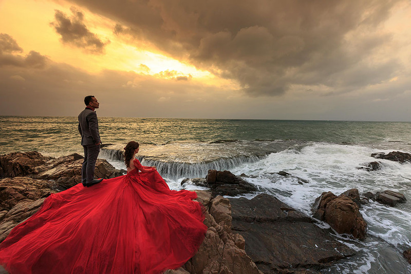 Bride and groom pose on a cliff by the ocean 