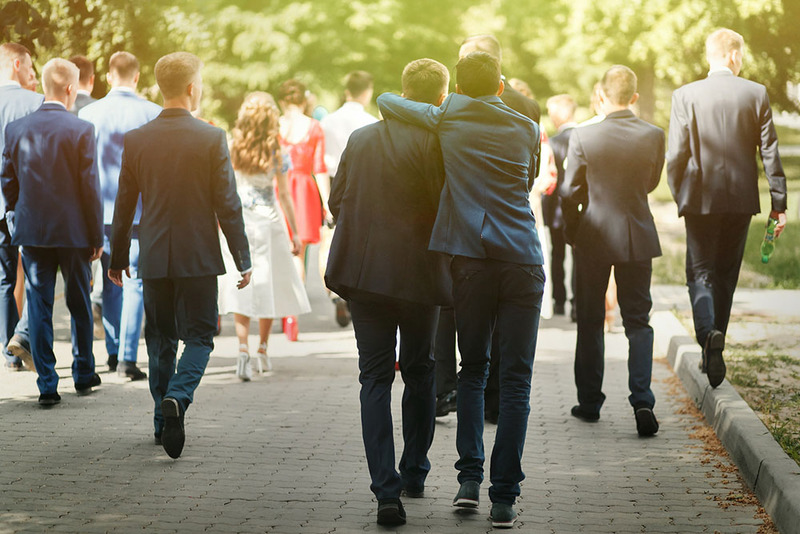 A group of friends and family members walk outside after a wedding ceremony, wearing suits and lovely dresses in the sunshine