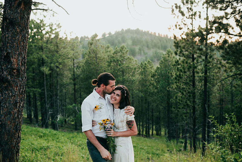 A bride and groom smile and hug outdoors in the forest on their wedding day