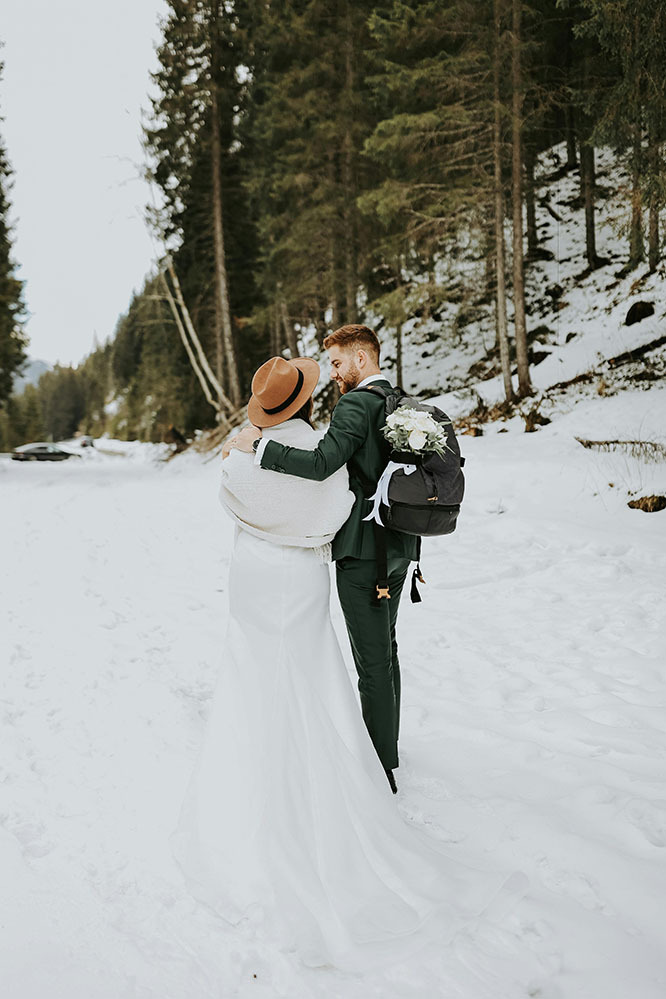 Bride and groom in snowy photos, groom carries a backpack
