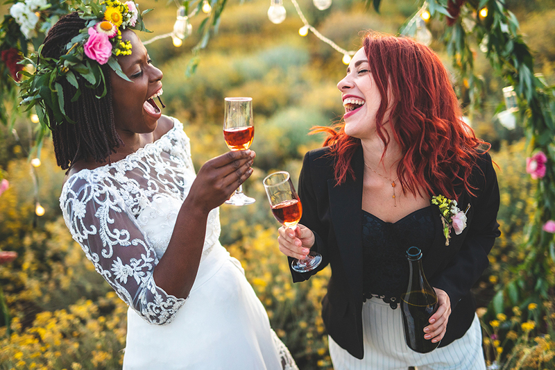 Two brides in flower headwreaths celebrate their wedding outdoors in a beautiful field on a sunny day