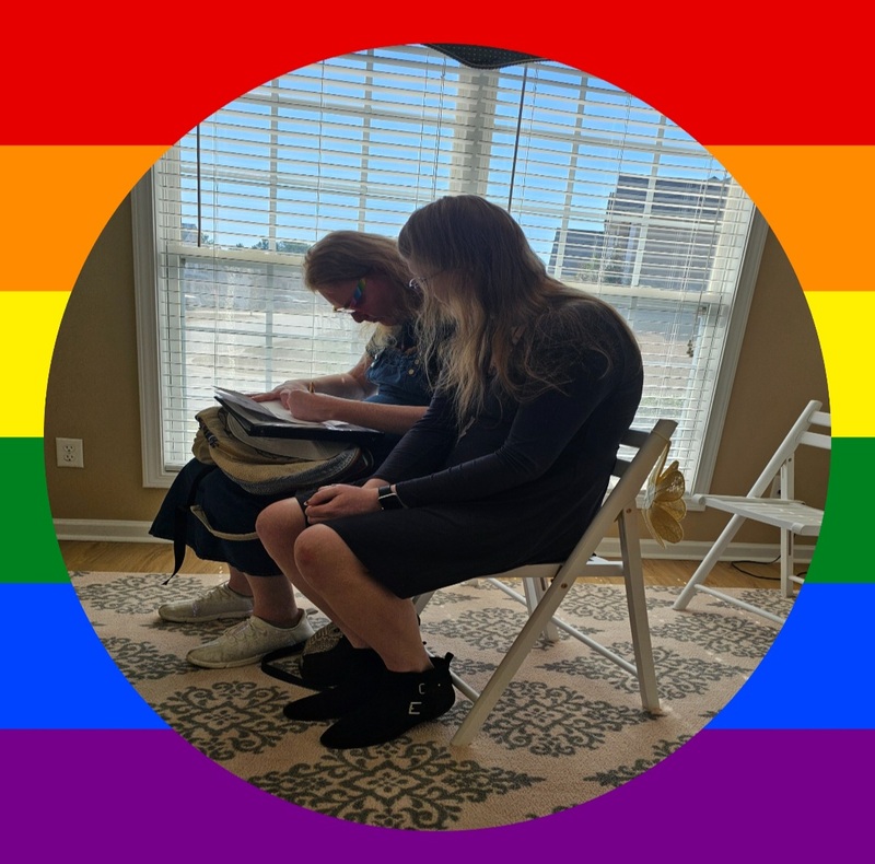 A couple signs a marriage license in Weddings w/TMS wedding room, the photo is framed with a colorful rainbow design symbolic of LGBTQ+ community