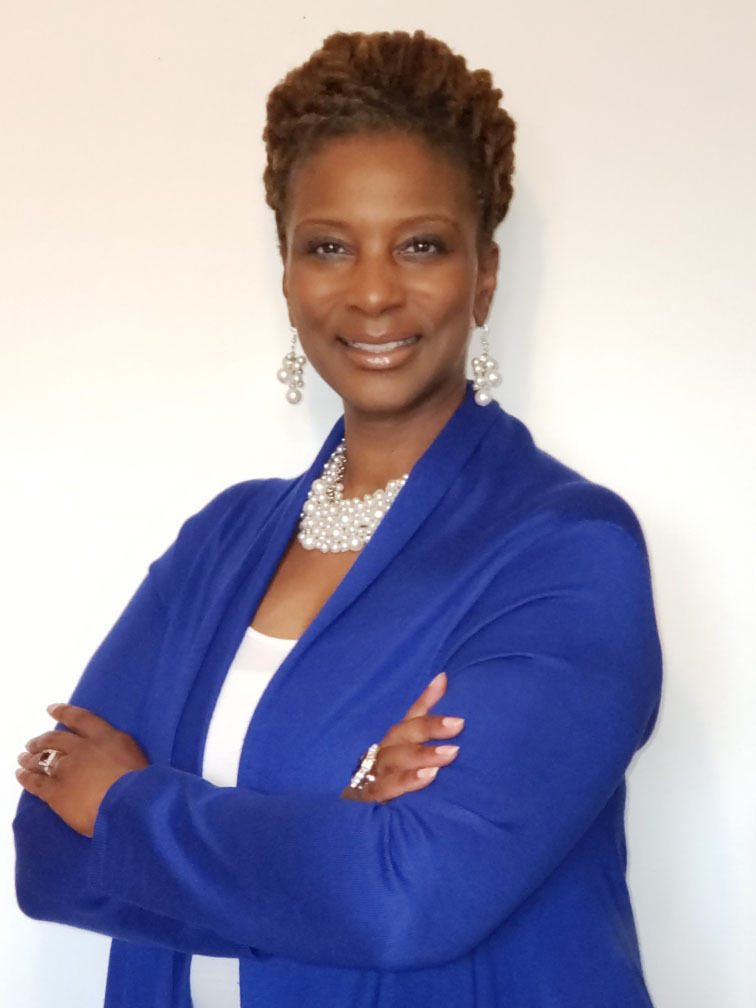 Minister Tiji Murphy looks toward the camera smiling, wearing a blue suit jacket