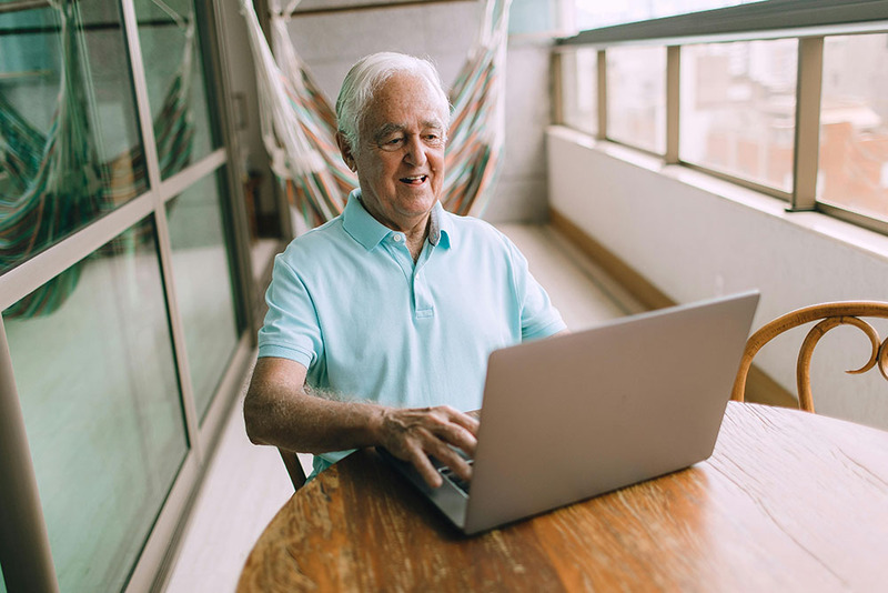 A man smiles while using his laptop at home, exploring his options for online ordination to officiate a wedding in Alaska! 