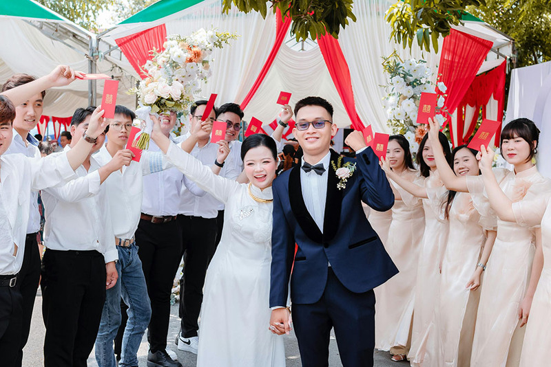 A joyful wedding outdoors, guests are holding out red envelopes for good luck to the bride and groom as their wedding gifts