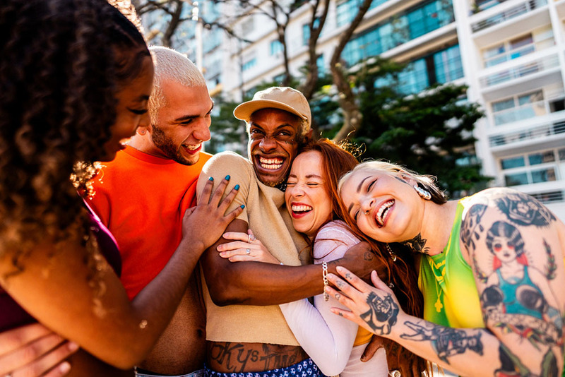 A group of friends gather around a newly ordained minister outside, hugging in the sunshine