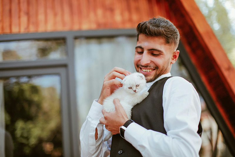 Groom poses while holding a cute white cat, smiling down at it