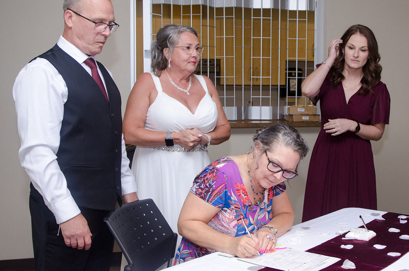 A non denominational minister signs the marriage license while the bride, groom, and bridesmaid watch