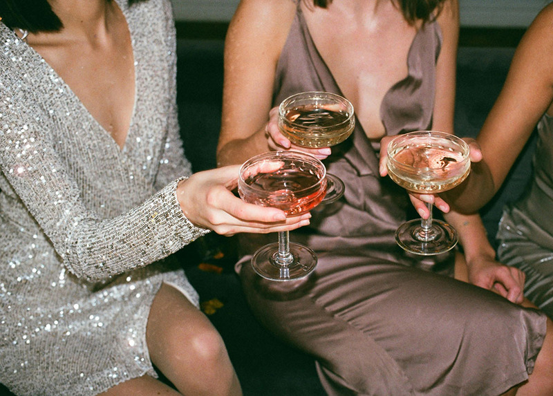 A close up of women in glittering gowns toasting cider