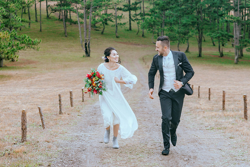 bride and groom run down a rural path smiling and happy, surrounded by trees