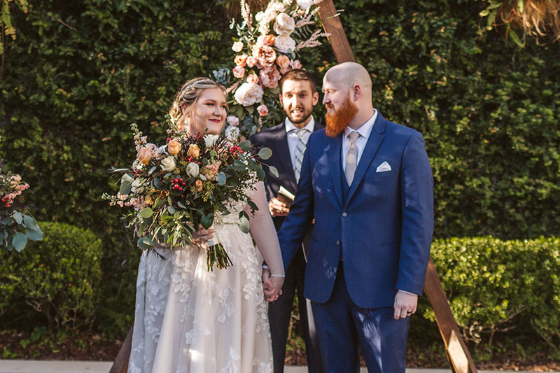 bride and groom hold hands and smile at each other as the wedding officiant introduces them 'married'