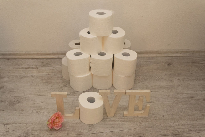 A tower of toilet paper with wood letters in front, spelling LOVE (with a roll of toilet paper as the 'o')