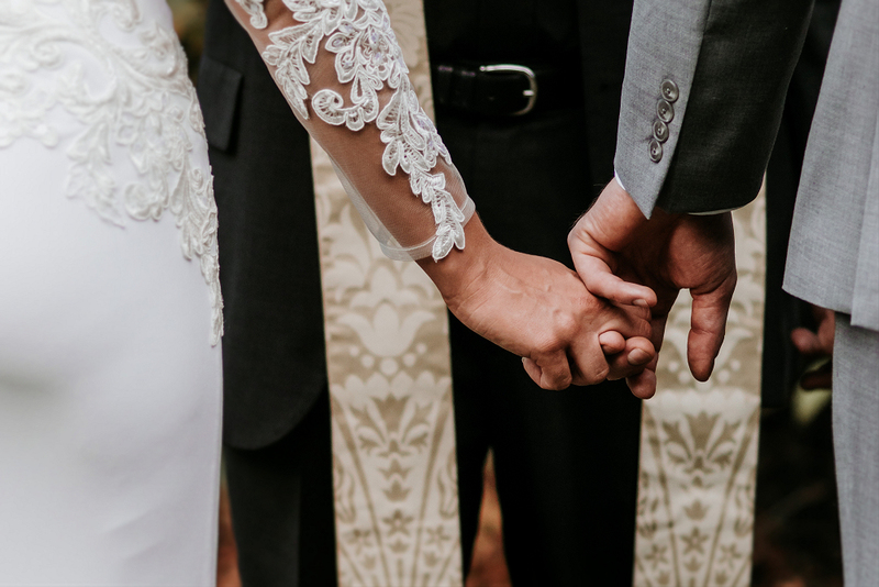 Partners clasp hands in front of the wedding officiant at their microwedding minimony ceremony during COVID-19