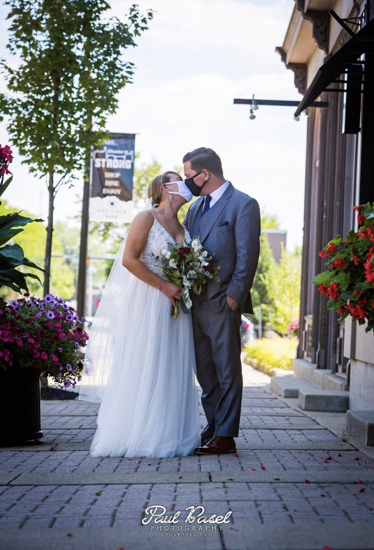 A bride and groom pose for photo on the wedding day, kissing in their decorative cloth masks
