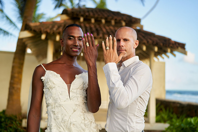 Two people hold up their hands to show their wedding rings, dressed in elegant attire