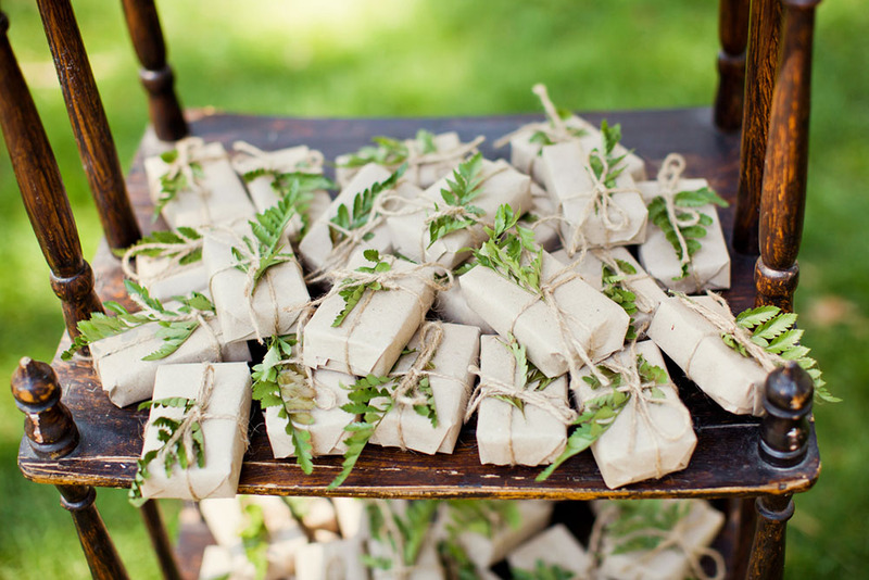 Outdoor table at a wedding, holding small boxes of wedding favors decorated with fern leaves