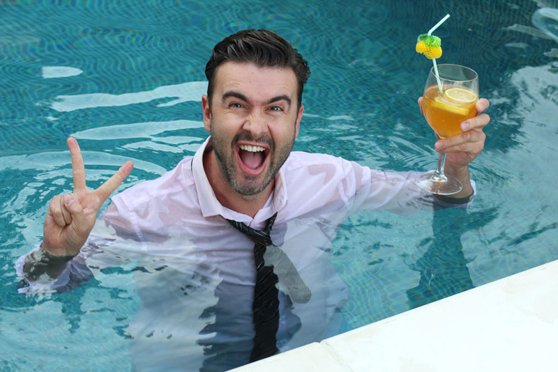 Man in a suit stands in a pool holding a cocktail