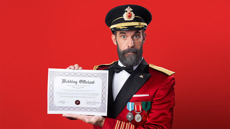 Captain Obvious poses in front of a red wall holding an ordination certificate