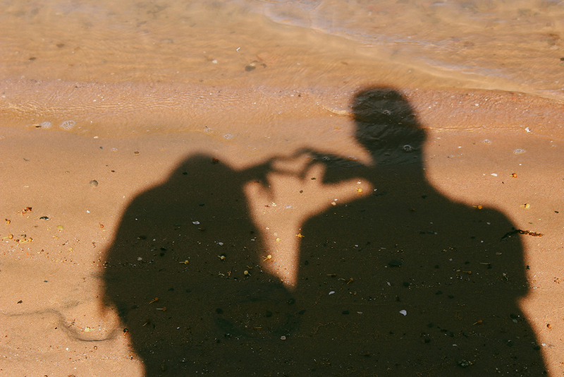 Couple makes the shape of a heart with the shadow of their hands in the sand at the beach