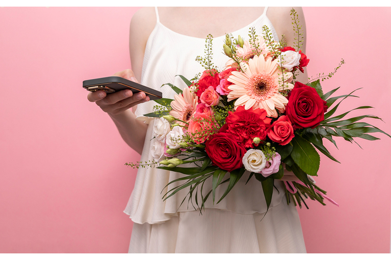 Woman in wedding dress holding bouquet and cellphone, symbolizes marriage to AI chatbot