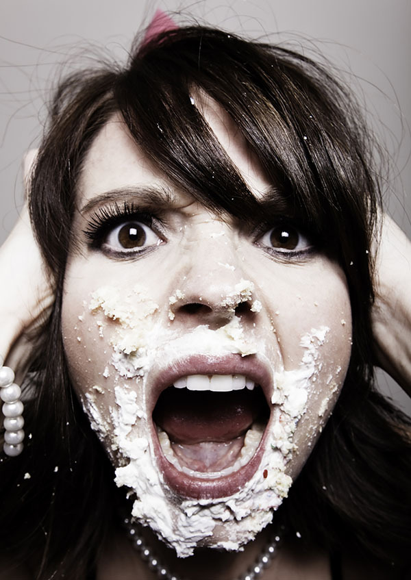 Close up of a bride screaming and angry, she has cake frosting all over her face