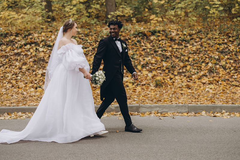 bride and groom walk along a road with colorful fall leaves