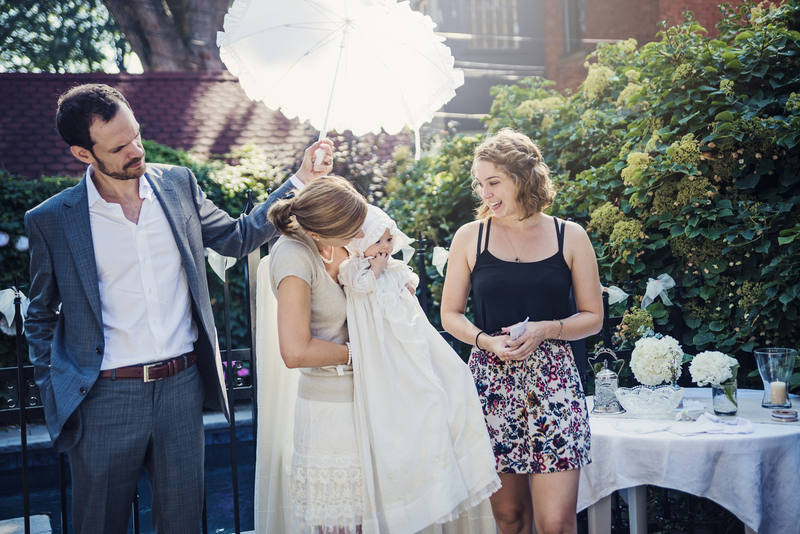 Minister and Parents pose with child at baptism, outdoors on sunny day