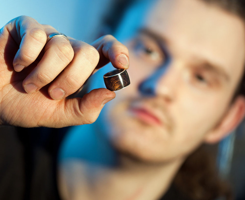 Man holds up a wedding ring made of wood and silver
