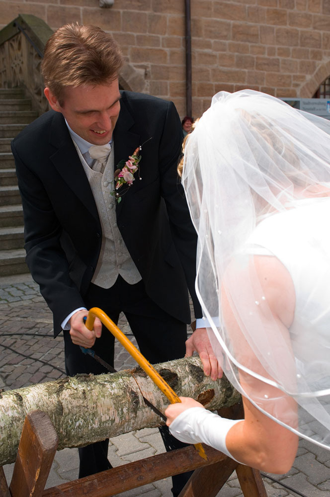 groom and bride work together to cut a log in half at the wedding using a two handled saw