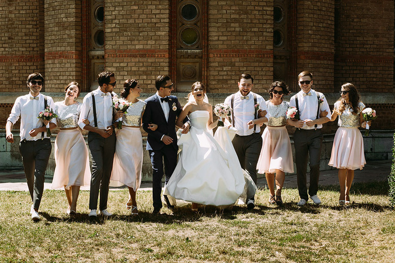 Las damas de honor, los padrinos de boda y los novios se paran en una larga fila, del brazo, sonriendo el día de la boda.