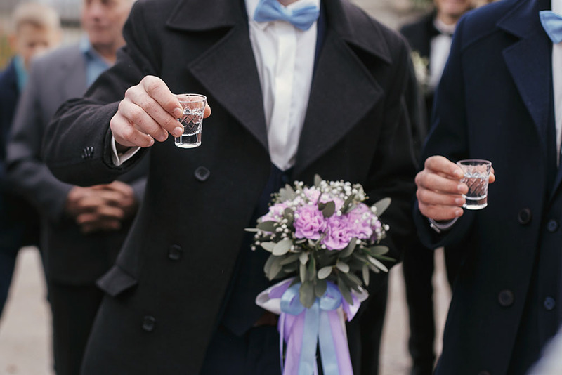 Close up of two grooms holding shots of vodka to toast
