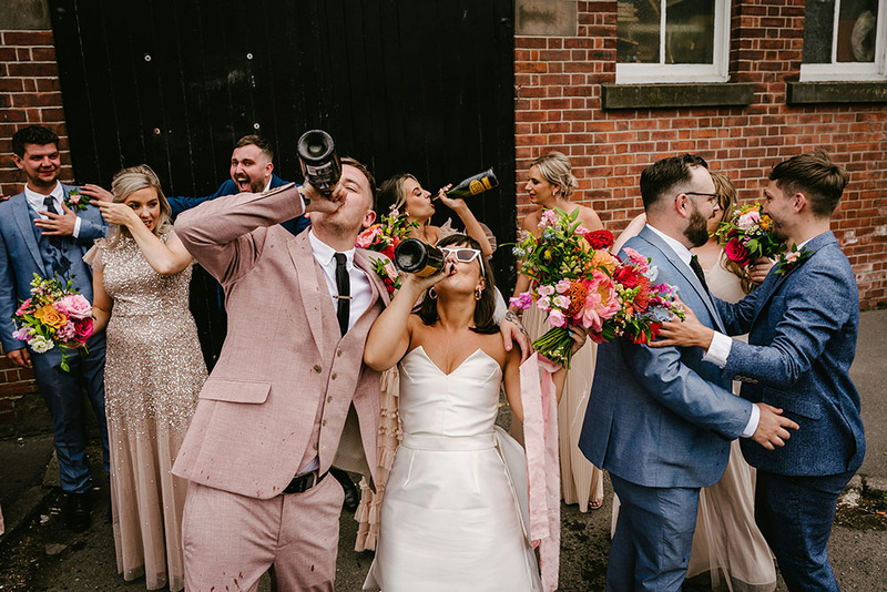 Festive wedding party, bride and groom drink from wine bottles