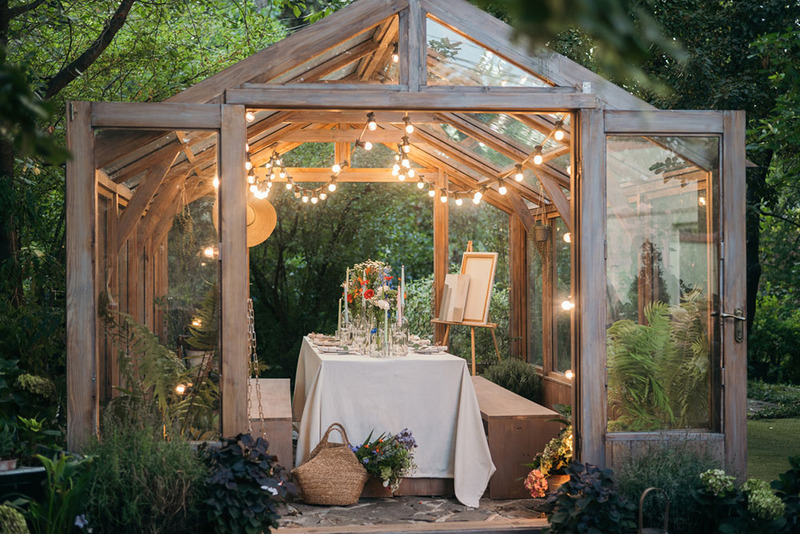 beautifully decorated glass greenhouse, set up for wedding with table, chairs, painting easel