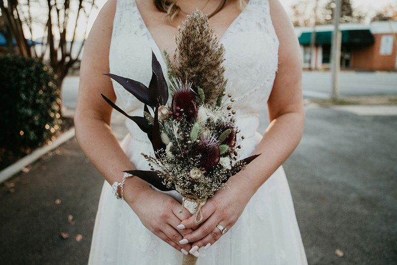 Close up of bride in white dress holding dried flowers bouquet