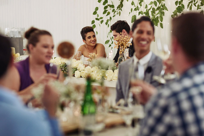 Wedding reception view, with guests at tables eating and drinking, newlyweds in background